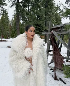 Detailed view of shaggy white faux fur long coat worn by a model in a snowy forest scene