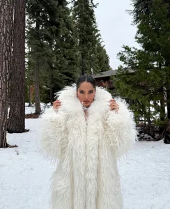 Detailed view of a long white shaggy faux fur coat worn in a snowy winter forest.