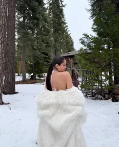 Close-up back view of a thick white long faux fur coat in a snowy forest landscape.