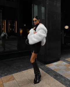 Elegant woman posing in a luxurious white faux fur coat against an urban architectural background