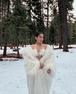 Full-length view of a white long-hair faux fur coat in a snowy forest setting.