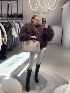 Stylish woman wearing an oversized brown curly faux sheep fur coat in a boutique mirror