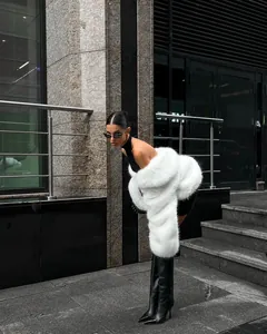 Side view detail of a fluffy white faux fur coat styled with black leather boots.