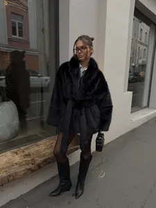 Lifestyle-Foto einer Frau in einem schwarzen Kunstpelzmantel mit Gürtel im Stadtzentrum.