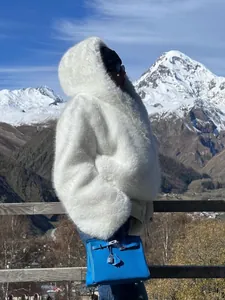 Manteau en fausse fourrure blanche à capuche dans un paysage de montagne enneigé