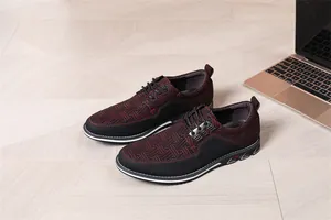 Herrenschuhe im englischen Stil mit rot-schwarzem Muster auf dem Boden neben Laptop