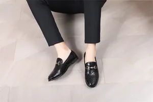 Detailaufnahme von schwarzen Loafern aus Leder mit Metallverzierung auf hellem Boden.