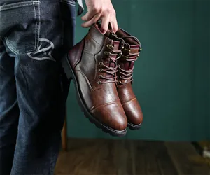 Close-up of vintage brown leather Martin boots held by hand for men's fashion