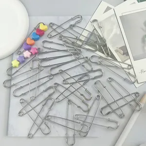 Close-up view of multiple large silver safety pins and one decorated with colorful heart beads.