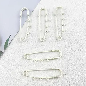 Close-up of white painted large safety pins with loops for DIY charms