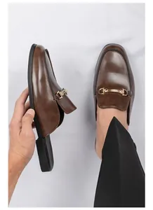 Vista detallada de mocasines tipo mule de cuero marrón para hombre con bocado dorado.