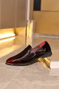 Side view of high-glossy patent leather loafers in burgundy resting on a gold book