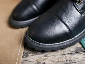 Detailed close-up of black leather boot toe showing precise stitching and lug sole