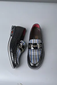 Detalle de mocasines de hombre en cuero negro texturizado con cuadros y bocado de metal dorado.