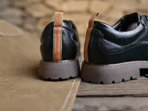 Nahaufnahme der Rückansicht schwarzer Herren-Derbyschuhe mit orange gestreiften Schlaufen.