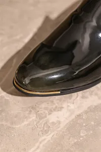 Close-up detail of luxury black patent leather men's shoe with gold metallic toe accent