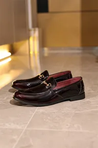Nahaufnahme glänzender burgunderroter Herren-Slipper aus Lackleder mit Trense