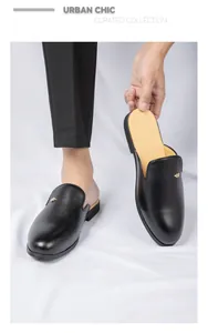 Detalle de mules de cuero negro para hombre con adorno metálico dorado.