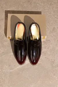 Top-down view showing glossy burgundy gradient men's dress loafers on stone background.