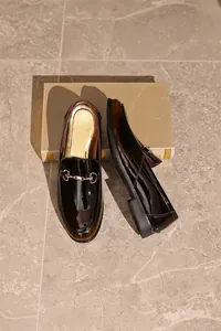 Draufsicht auf hochwertige braune Lackleder-Loafer für Herren auf einem beigen Ständer