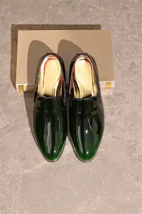 Detailed top-down view of luxury men's dark green patent leather loafers on stone floor