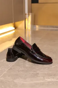 Detaillierte Nahaufnahme von dunkelroten Lackleder-Loafers auf elegantem Marmorboden