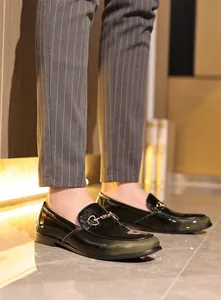 Detailaufnahme herren loafer aus lackleder in schwarz und grün mit goldener schnalle.