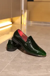 Side view detail of shiny dark green patent leather loafers with golden metal trim
