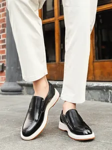 Close-up of men's black leather loafers with stylish thick white soles in outdoor setting.