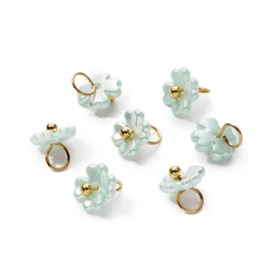 Macro view of 3D pearlescent flower charms with golden loops for DIY jewelry making.
