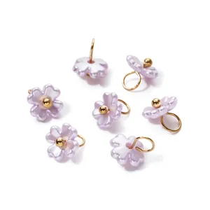 Macro detail of iridescent pearl flower charms with gold loops for DIY jewelry making.