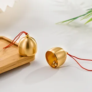 Close-up of minimalist matte brass bell pendants with red strings on wooden tray