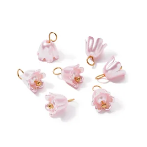 Macro view of iridescent pink pearl lily flower charms with gold loops for DIY jewelry.