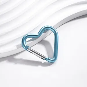 Gros plan d'un mousqueton en aluminium bleu en forme de cœur sur un fond blanc épuré.