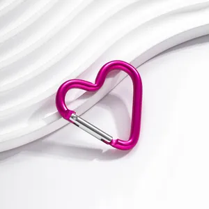 Gros plan d'un mousqueton en aluminium rose en forme de cœur sur fond blanc.