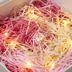 Primo piano di carta triturata rosa e crema per confezioni regalo con luci a LED