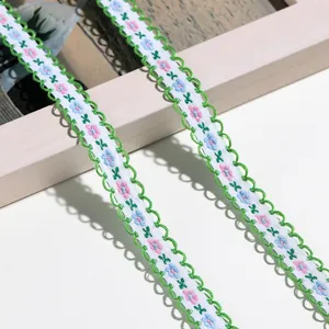 Detailaufnahme von zarter floral bestickter Spitzenborte mit grünem Wellenrand