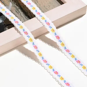 Nahaufnahme von weißem besticktem Spitzenband mit bunten Blumenmustern und Wellenkante