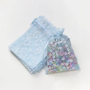 Detail van lichtblauwe organza tassen met trekkoord, witte bloemenprints en kralen