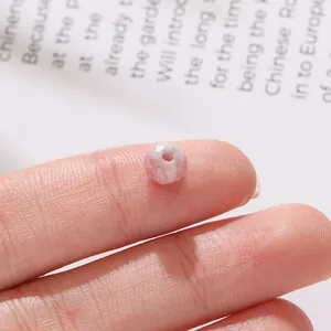 Makro-Detailansicht einer 6 mm facettierten rosa wassergefärbten Glasperle auf der Fingerspitze