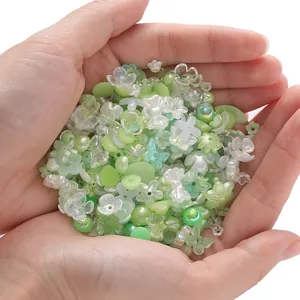 Hand holding a variety of green and white floral acrylic beads for DIY jewelry making.