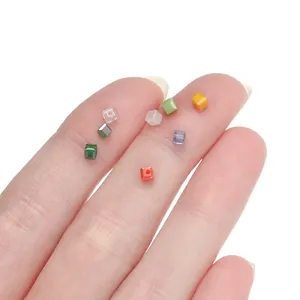 Perle di vetro colorate a cubetto macaron sulle dita per scala e dettaglio visivo