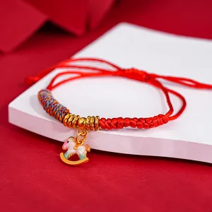 Macro detail view of a traditional red braided bracelet with a golden rocking horse charm