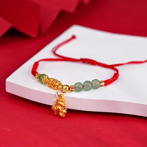 Close-up of red braided cord bracelet with gold horse pendant and green translucent beads