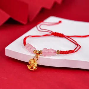 Close-up detail of a red string bracelet featuring a gold rocking horse and pink beads