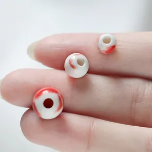 Detailed macro view of handmade white ceramic beads with red wash patterns for jewelry