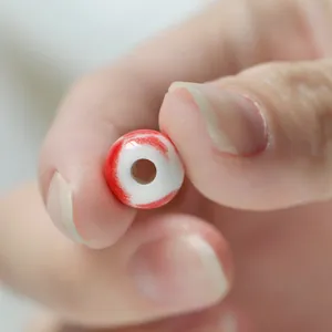 Close-up of a handmade red and white ceramic bead held by fingers for DIY jewelry