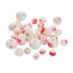Detailed view of round white ceramic beads with red ink patterns for jewelry DIY.