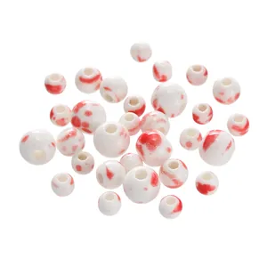 Close-up of white ceramic beads with red splatter patterns for DIY jewelry crafts.
