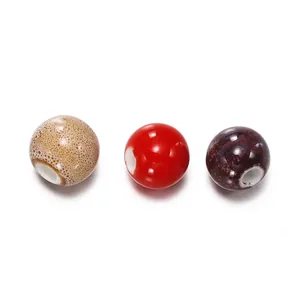 Detailed view of three round ceramic beads in red, speckled tan, and mottled purple colors.
